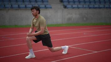 An athlete is stretching on the track field as part of their warmup before competing video