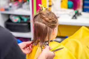 Close up view of hairdresser hands making a hair style to cute little girl in real child salon with colorful interior and toys. High quality photo