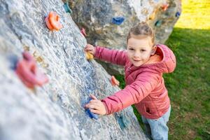 Little girl climbing an artificial climbing wall in a playground, developing strength and coordination. High quality photo