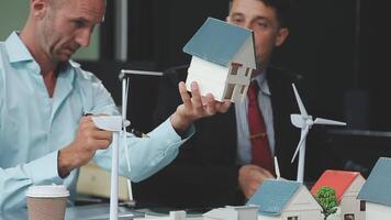 Two men are looking at model houses and wind turbines video