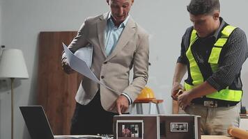 Two men in safety vests and hard hats working on a model of a house video