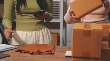 Two women are standing in front of boxes and a laptop video