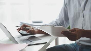 A man is sitting at a desk with a clipboard and laptop video