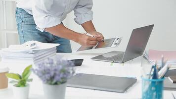 A man is working on a laptop while holding a clipboard video