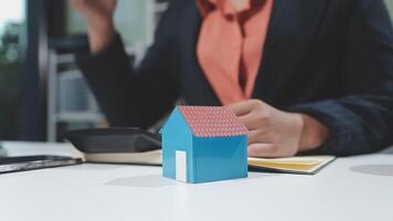 A woman is holding a house model in front of her laptop video