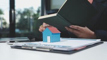 A woman is reading a book and holding a house model on a desk video