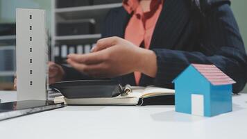 A woman is holding a house model in front of a laptop video