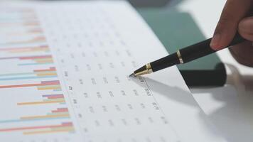 A person's hand holding a pen and pen is pointing at a graph video