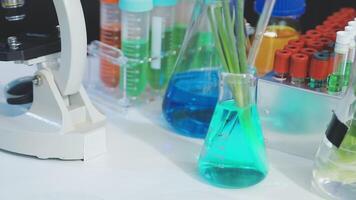 A microscope, a vase with green liquid, and a glass vial video