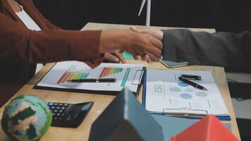 Two people shaking hands over a desk with papers and a globe video