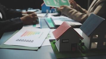 A couple of people are sitting at a table with a house model video