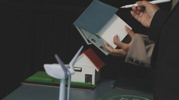 A man is holding a paper house and a wind turbine video