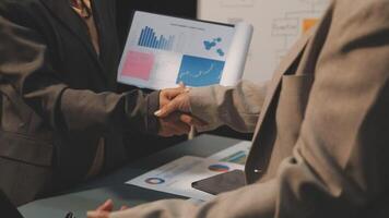 Two business people shaking hands over a table with graphs and papers video
