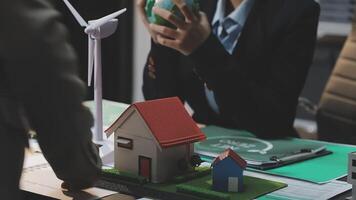 A man and woman are sitting at a table with a house and wind turbine video