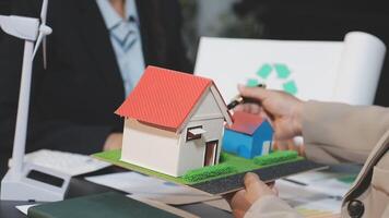 A man is holding a model of a house and a recycling bin video