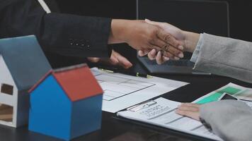 Two people shaking hands over a table with a house model video