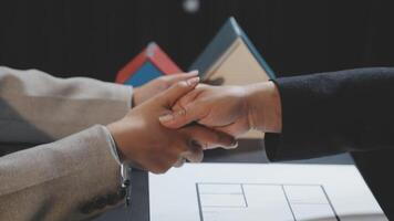 Two people shaking hands over a table with a house model video