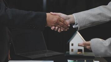 Two business people shaking hands over a desk with a house model video