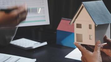 A person holding a house model in front of a computer video