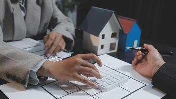 Two people are working on a house model with a calculator video