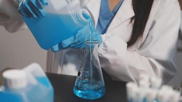A woman in a lab coat is pouring blue liquid into a beaker video
