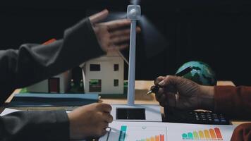 Two people are working on a laptop with a wind turbine video