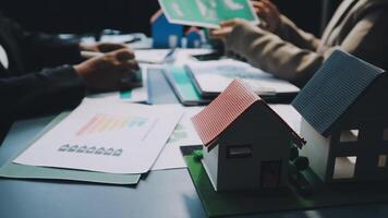A couple of people are sitting at a table with a house model video