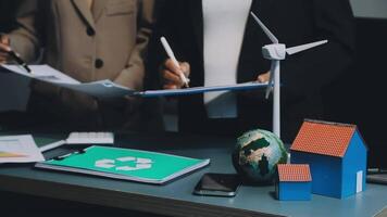 Two people are working on a desk with a wind turbine video