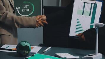 Two people shaking hands over a table with a net zero logo video