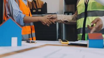 Two construction workers shaking hands over a table with a house video