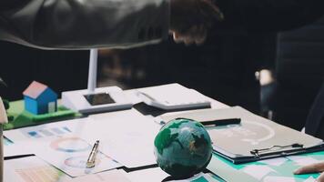 Two people shaking hands over a table with papers and a globe video