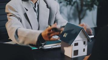 A man and woman are sitting at a table with a house model video