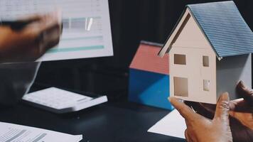 A person holding a model of a house in front of a computer video
