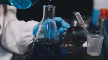 A person in a lab coat pouring liquid into a beaker video