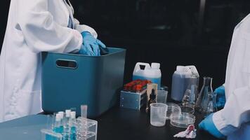 Two people in lab coats and gloves are working on a table video