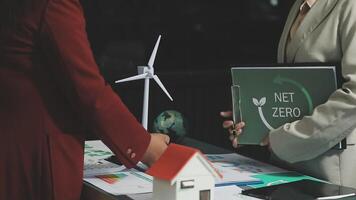 Two business people standing next to a table with a net zero sign video