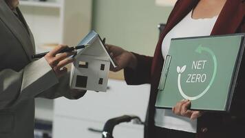 Two people holding a house model and a net zero sign video