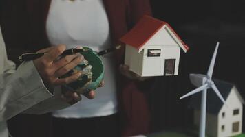A man holding a model of a house and a wind turbine video