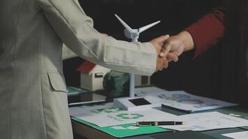 Two business people shaking hands over a table with wind turbines video