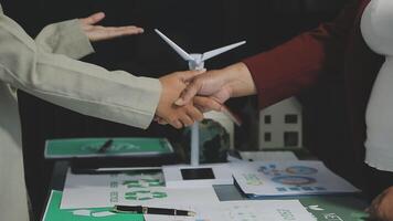 Two people shaking hands over a table with wind turbines video