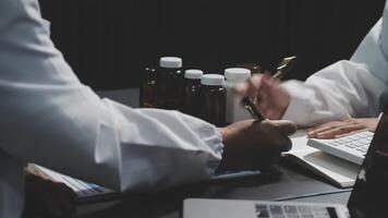 Two people in lab coats sitting at a table with a laptop video