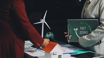 Two people standing next to a table with a net zero sign video