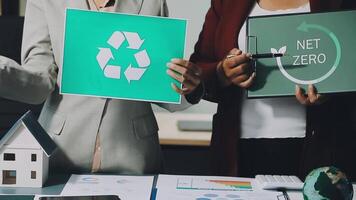 Two people holding up signs with recycling and net zero video