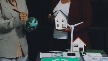 Two people holding paper houses and a wind turbine video