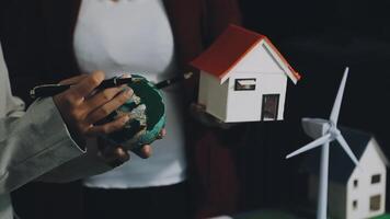 A man holding a model of a house and a wind turbine video