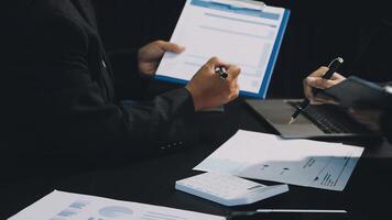 Two people sitting at a table with papers and a laptop video