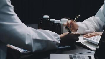 Two people in lab coats sitting at a table with a laptop video