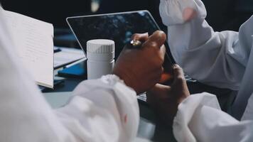 Two people in white lab coats are holding a tablet video