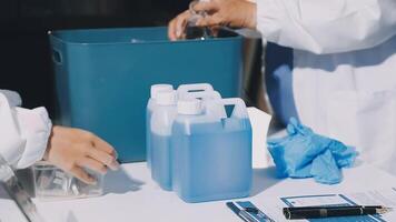 Two people in lab coats are working on a table with bottles and a container video