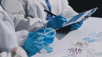 Two people in lab coats and gloves are working on a clipboard video